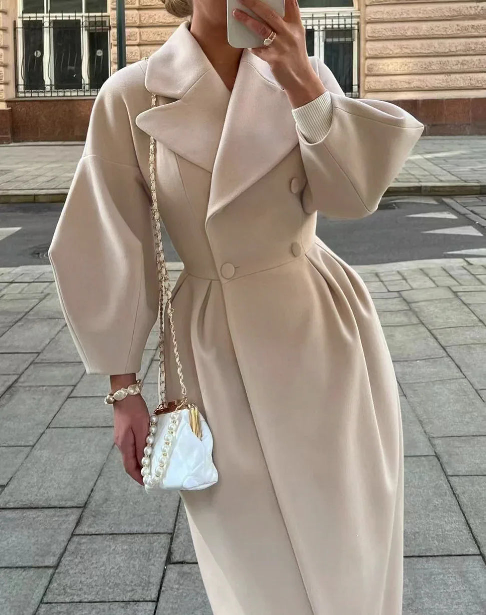 Woman wearing beige double-breasted coat with wide lapels and voluminous sleeves, holding a pearl-accented white handbag on city sidewalk