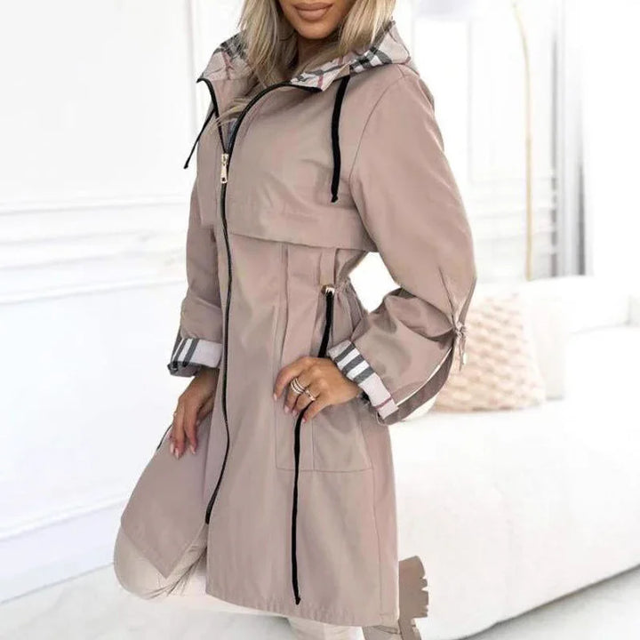Woman wearing stylish beige trench coat with striped cuffs and black drawstring zipper