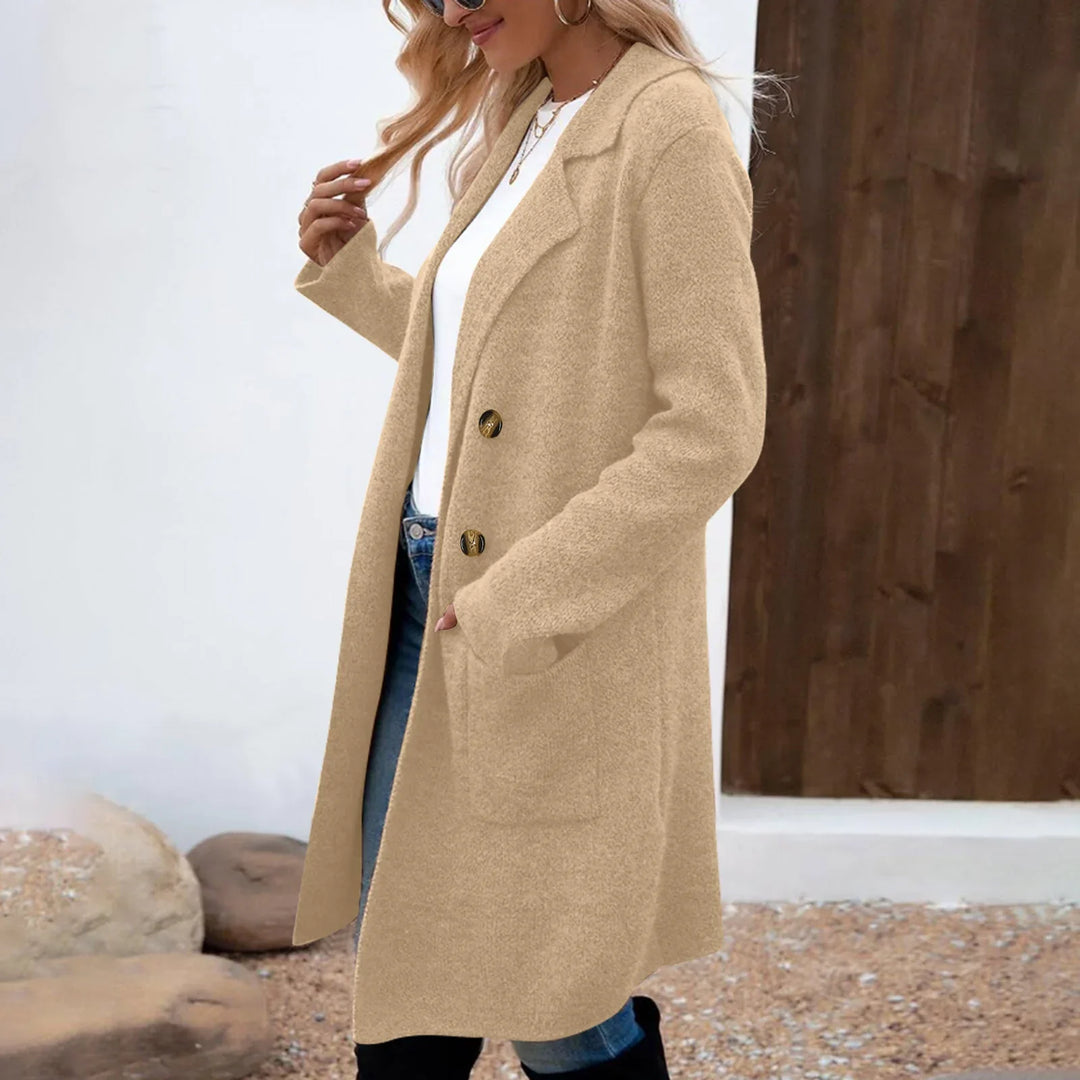 Woman wearing a beige wool coat with buttons, white shirt, blue jeans, and sunglasses outdoors