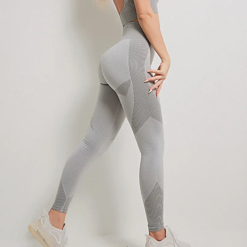 Woman wearing seamless gray textured leggings and white sneakers posing against a white wall