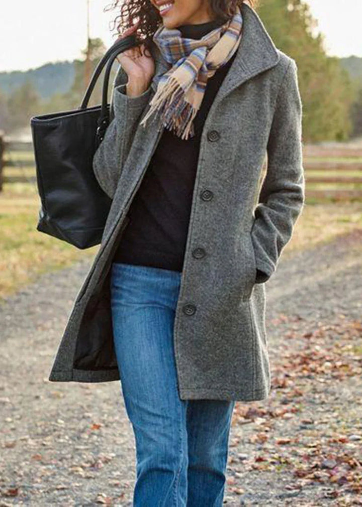 Woman wearing a gray wool coat, plaid scarf, blue jeans, and carrying a black tote bag outdoors