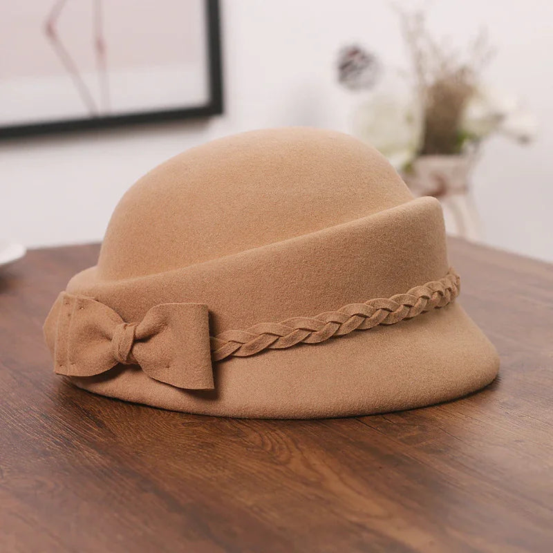 Beige felt cloche hat with braided band and bow detail on wood table