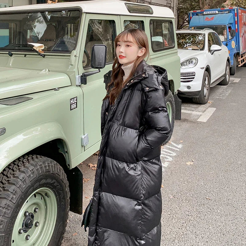 Woman wearing long black puffer coat standing next to a light green vintage off-road vehicle on a city street