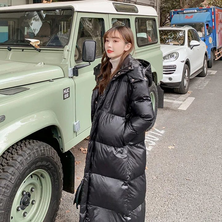 Woman wearing long black puffer coat standing next to a light green vintage off-road vehicle on a city street