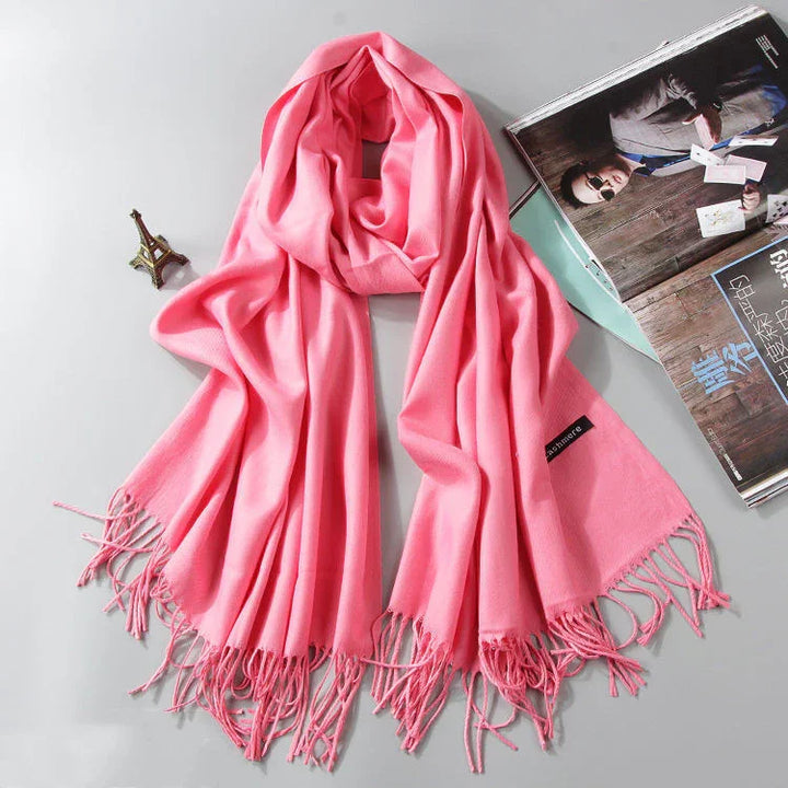 Soft pink cashmere scarf with fringes laid out next to a small Eiffel Tower figurine and open magazine
