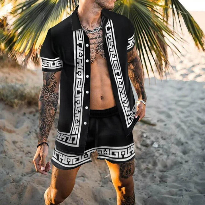 Man wearing black short-sleeve shirt and shorts with white geometric patterns on sandy beach under palm leaves