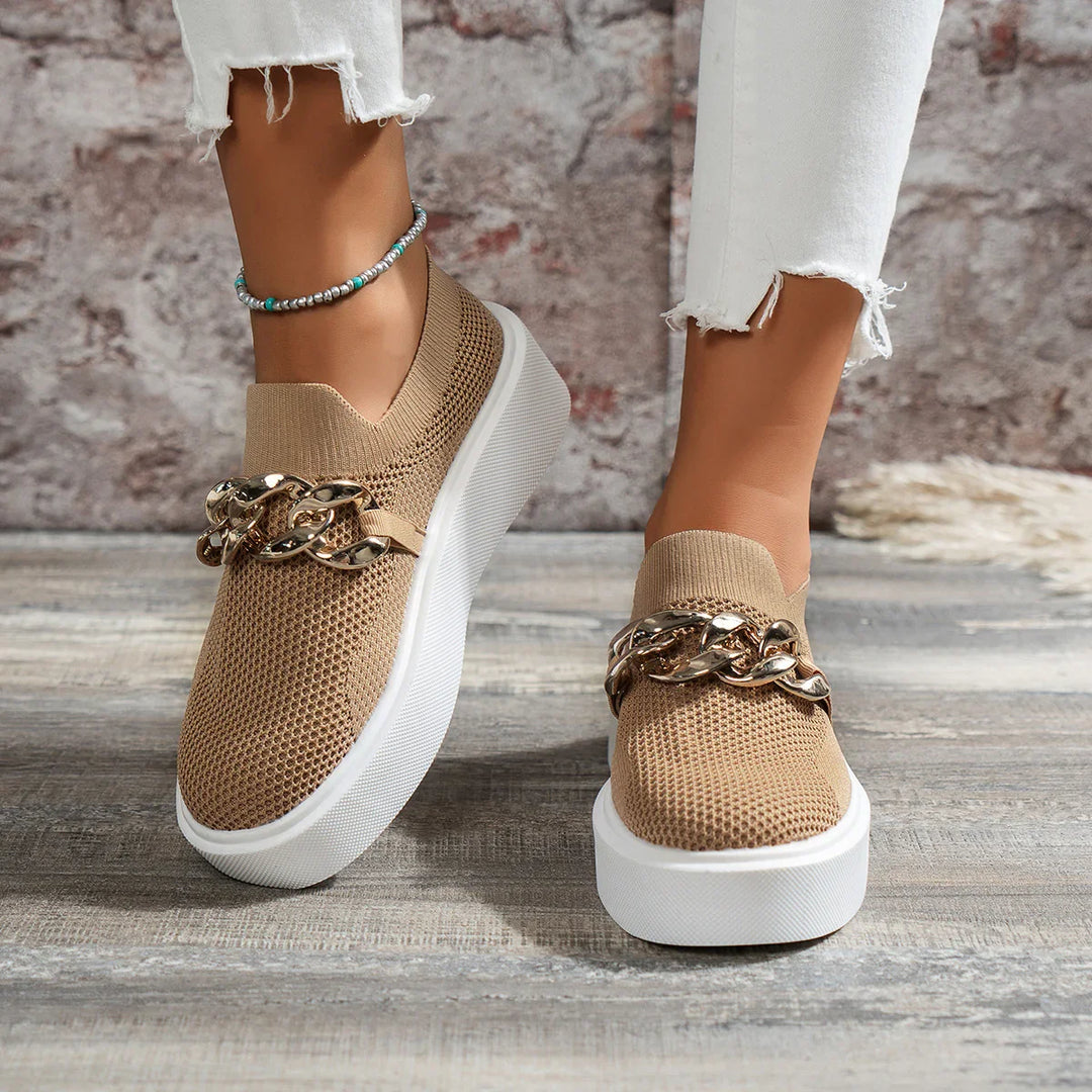 Beige slip-on knit sneakers with chunky gold chain detail, worn with white distressed jeans