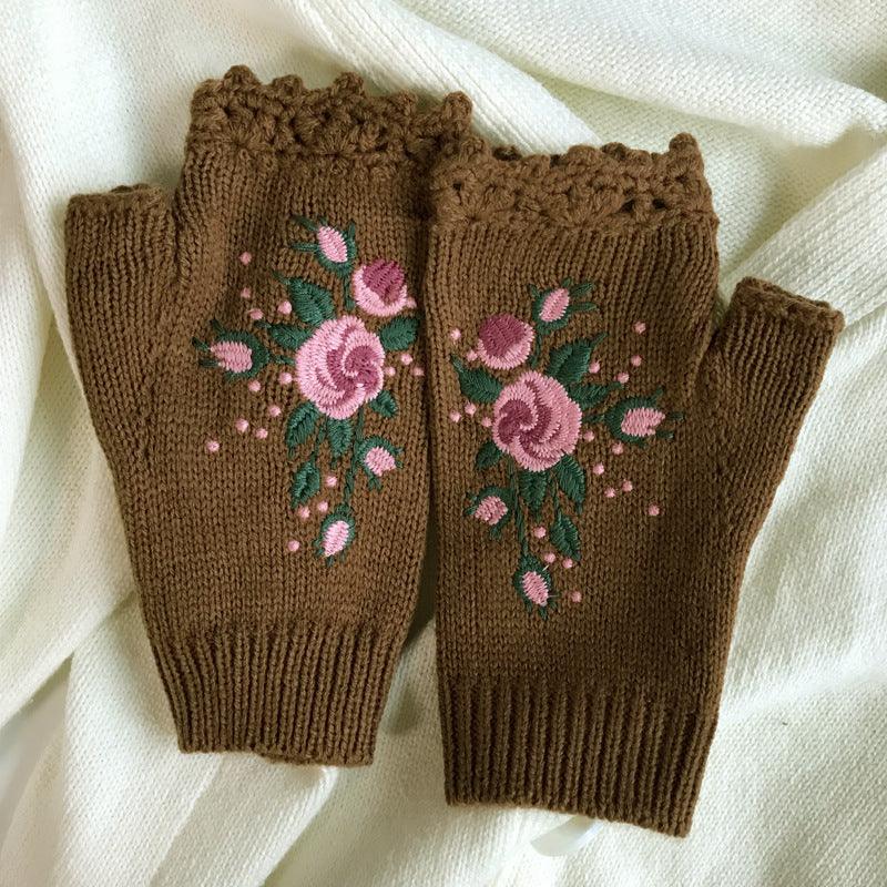 Brown knitted fingerless gloves with pink rose embroidery and green leaves on a white fabric background
