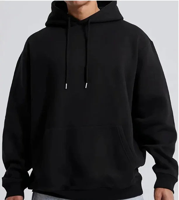Man wearing plain black oversized hoodie with front pocket and drawstrings against gray background