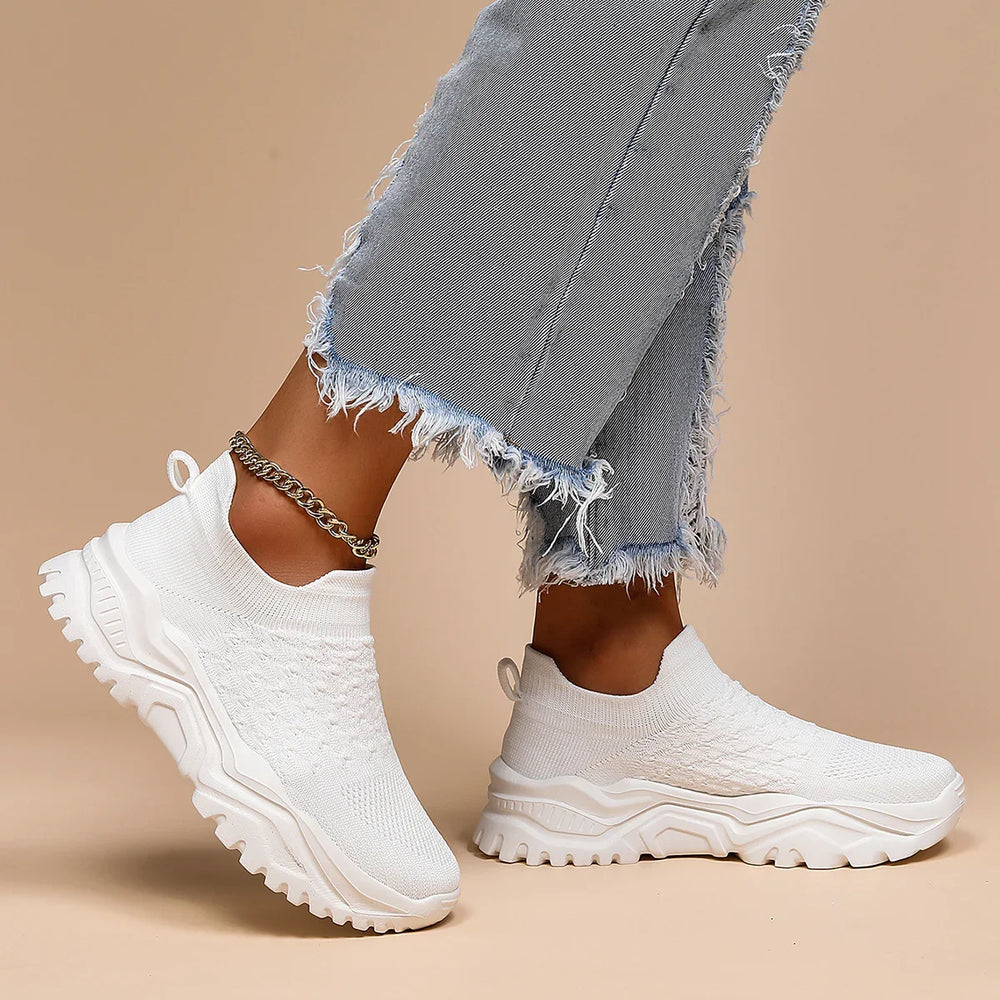 Close-up of white knit slip-on sneakers with chunky soles worn with frayed hem jeans and chain anklet