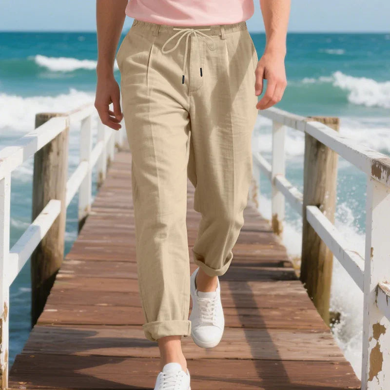 Man walking on wooden beach pier wearing beige linen pants and white sneakers