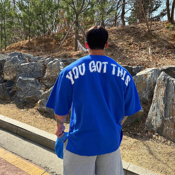 Man wearing blue t-shirt with 'You Got This' text outdoors near rocks and trees