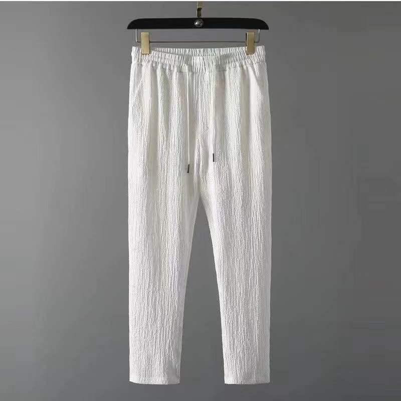 White textured casual pants with elastic waistband and drawstrings hanging on black hanger against gray background