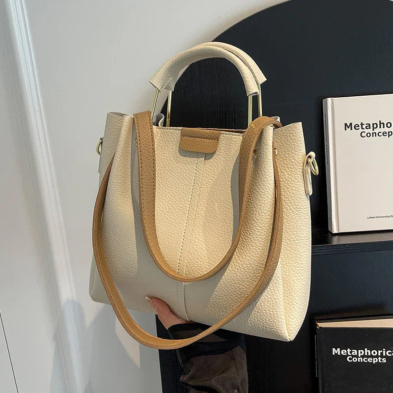 Cream leather handbag with tan straps held in hand against black shelves with books