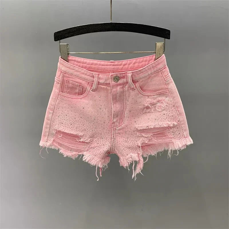Pink distressed denim shorts with frayed hem and small rhinestones hanging on black hanger
