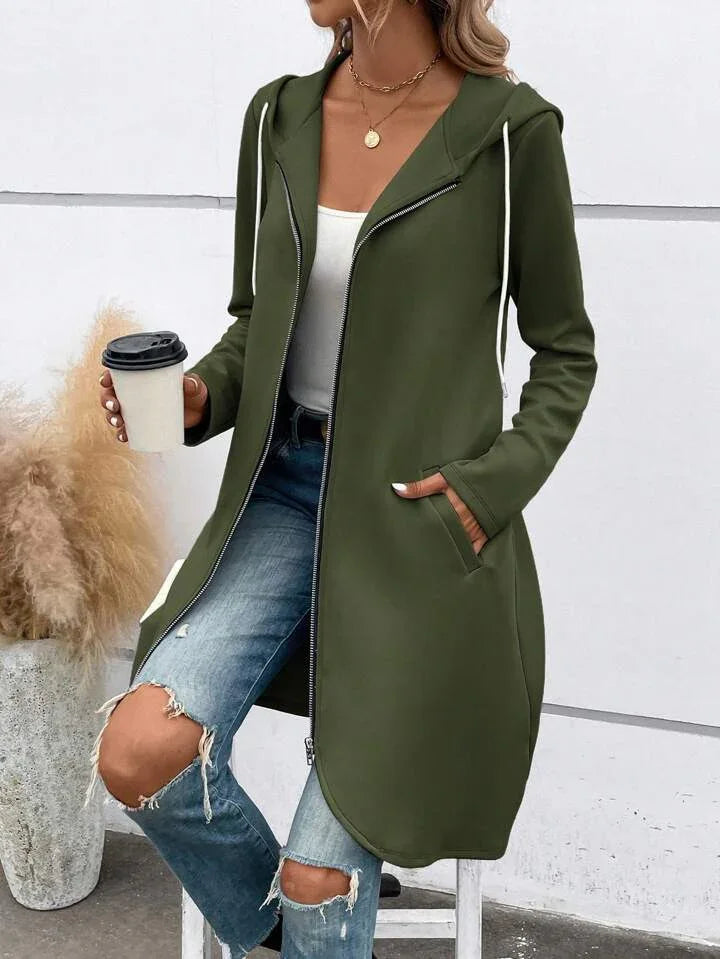 Woman wearing olive green long zip-up hoodie with white drawstrings, distressed blue jeans, holding coffee cup