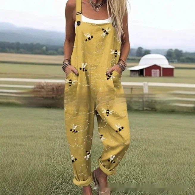 Woman wearing yellow bee print overalls standing in a grassy field with countryside barn in background