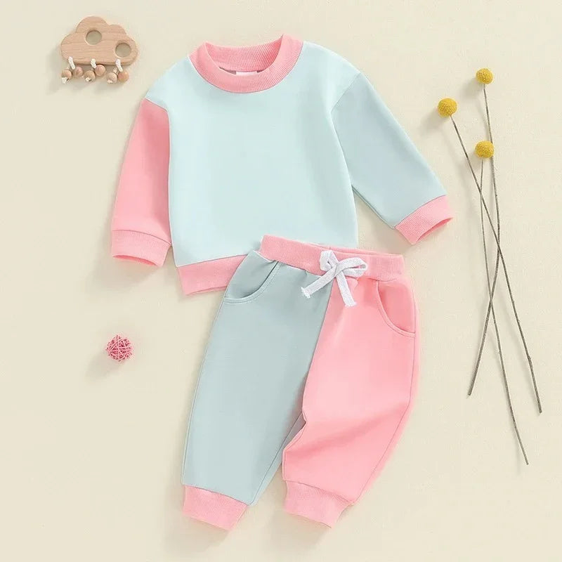 Two-tone pink and light blue baby toddler outfit with sweatshirt and pants on beige background