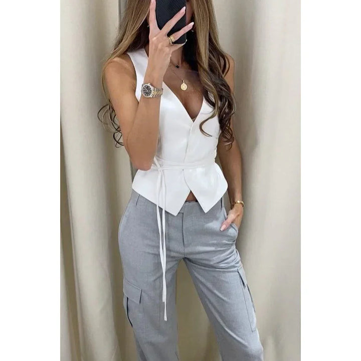 Woman in white sleeveless wrap top and light gray cargo pants taking mirror selfie