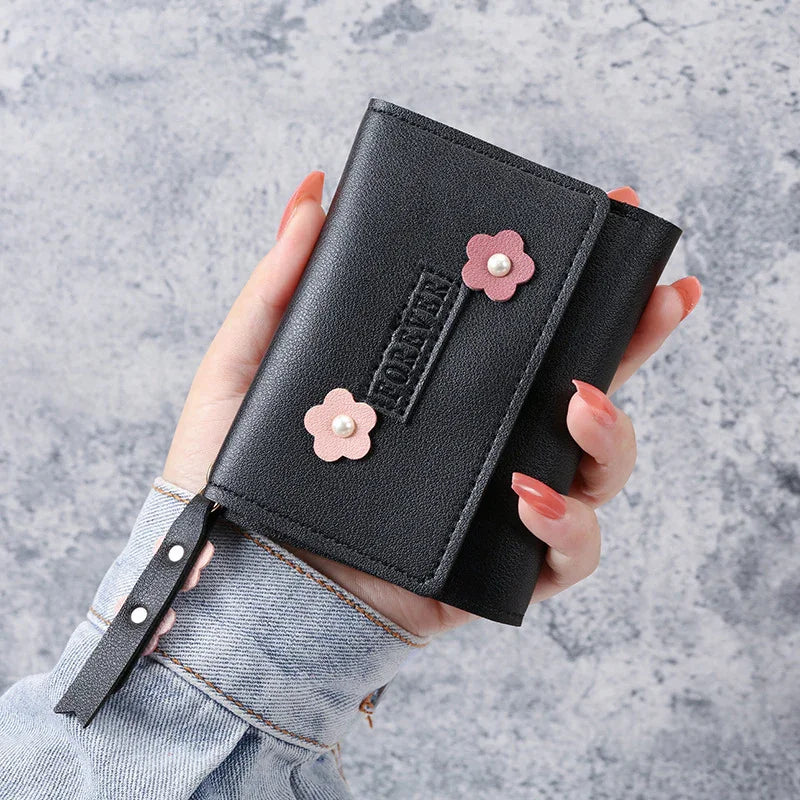 Hand holding black leather wallet with pink flower accents and pearl centers on gray background