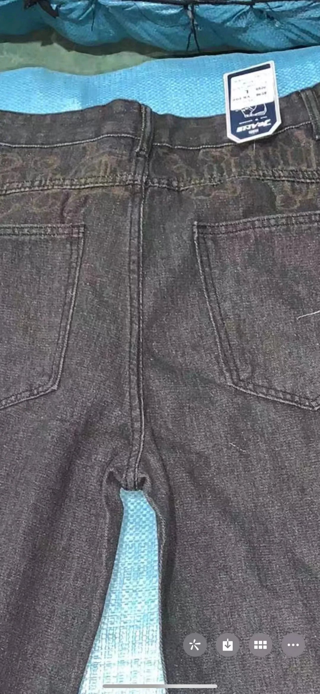 Back view of black denim jeans with tag on waistband laid on blue textured surface