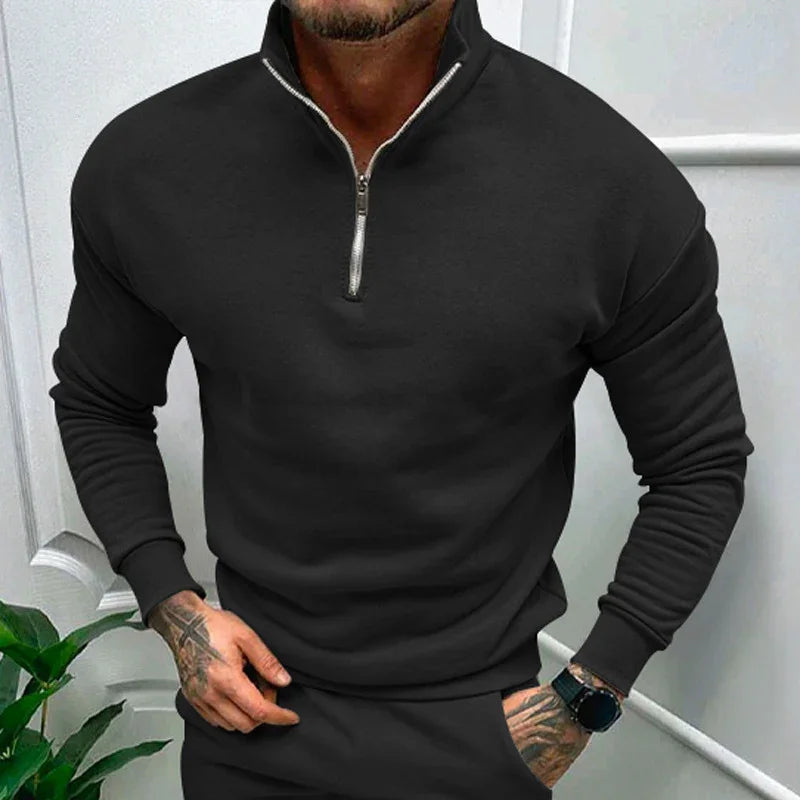 man wearing black half-zip sweatshirt and matching pants with tattooed hands and smartwatch