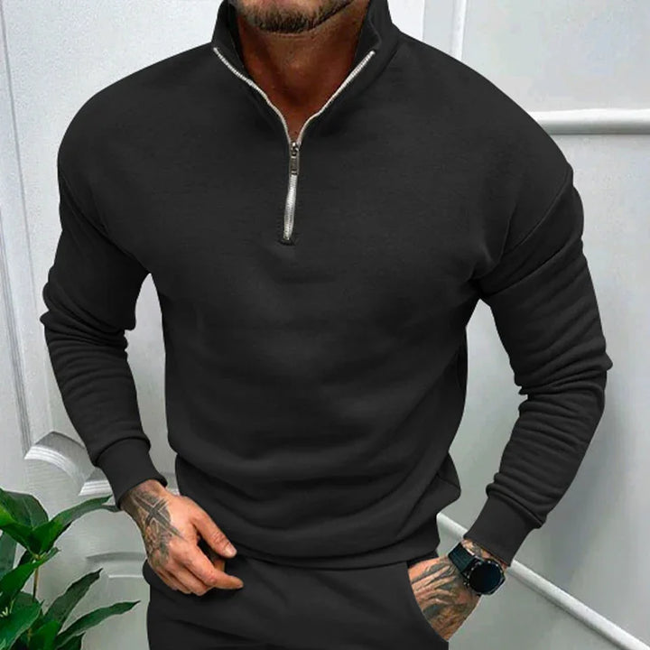 man wearing black half-zip sweatshirt and matching pants with tattooed hands and smartwatch