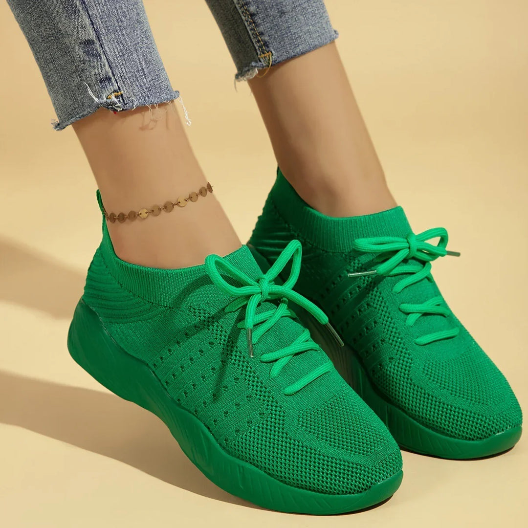 Close-up of feet wearing bright green knit sneakers with laces and cropped blue jeans on beige background