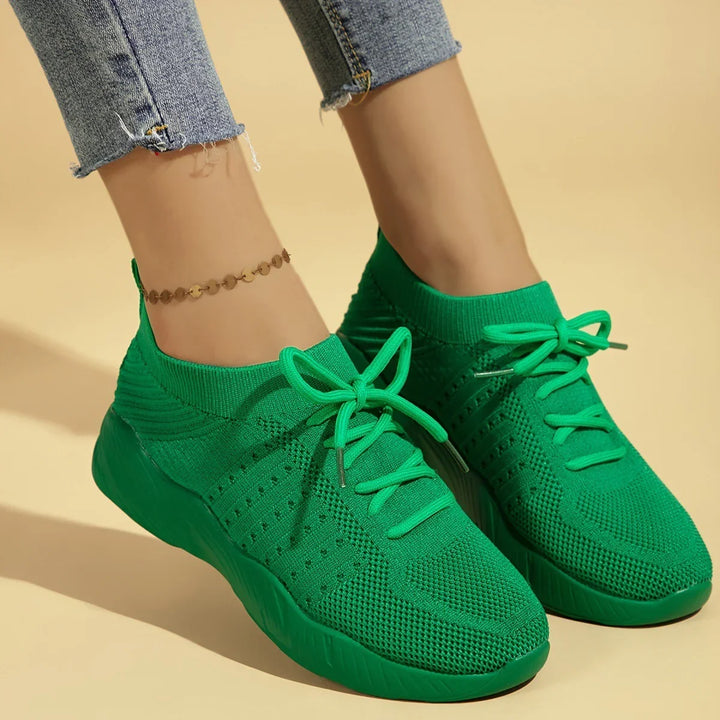 Close-up of feet wearing bright green knit sneakers with laces and cropped blue jeans on beige background