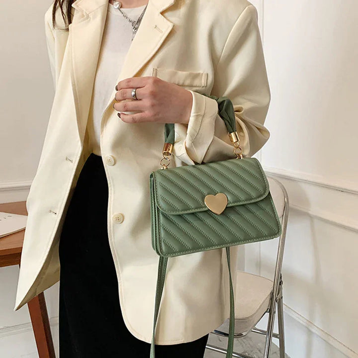 Woman wearing cream blazer holding green quilted handbag with heart-shaped gold clasp