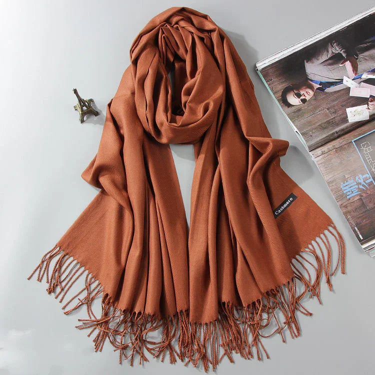 Rust brown cashmere scarf with fringed edges on white surface next to miniature Eiffel Tower and magazine