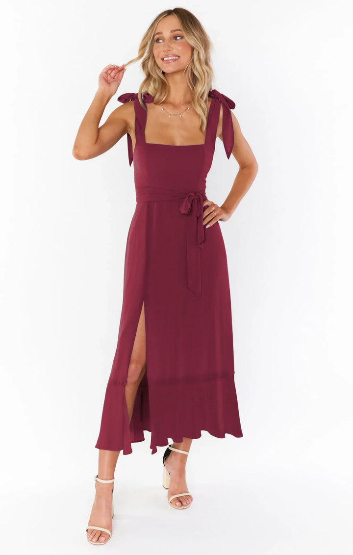 Woman wearing a sleeveless burgundy midi dress with shoulder ties and side slit, paired with beige block heels