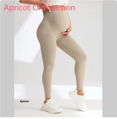 Pregnant woman wearing apricot-colored maternity leggings and white sneakers, standing against a light background