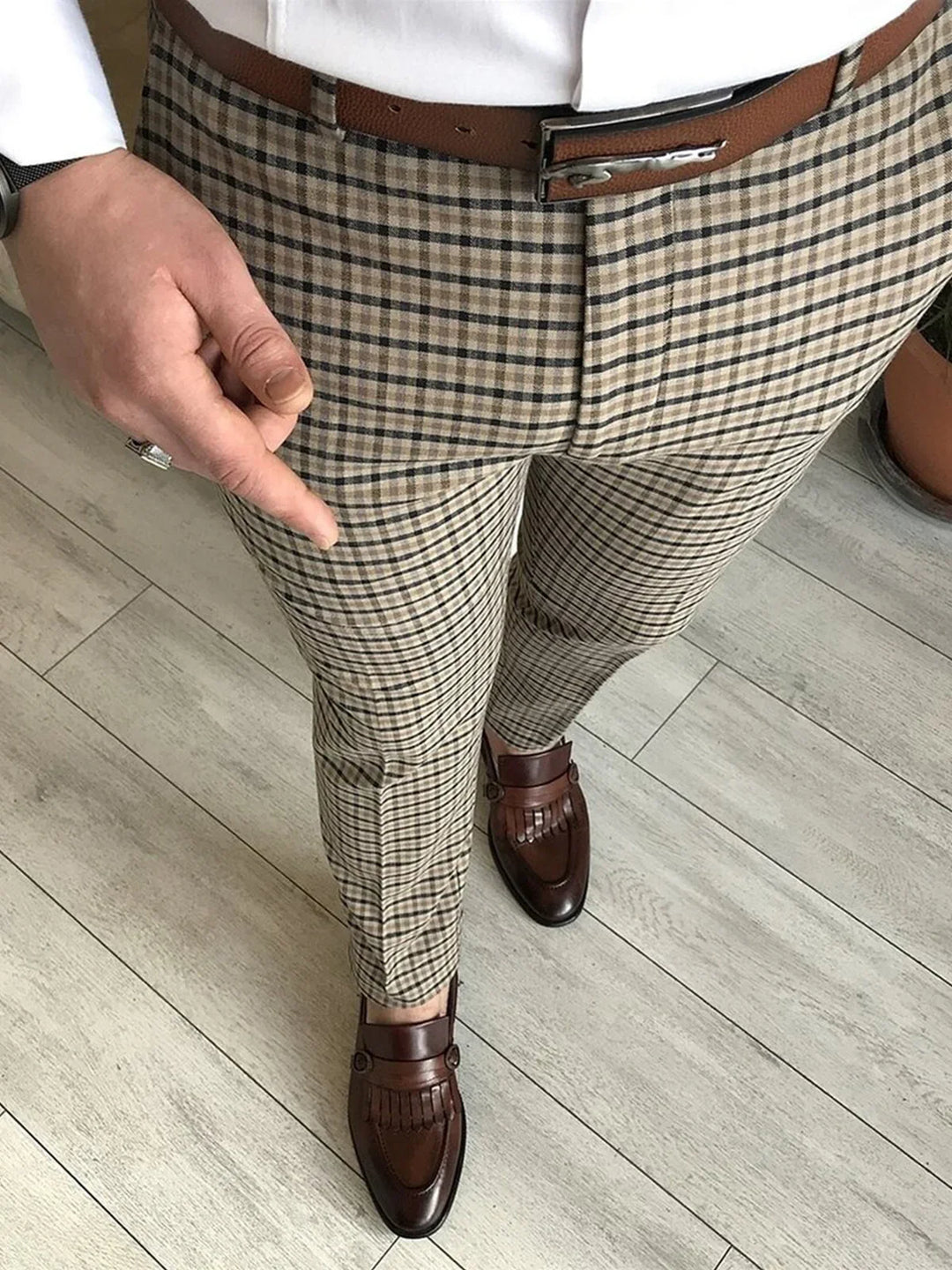 Man wearing beige plaid pants, brown leather belt, and brown tassel loafers on wooden floor