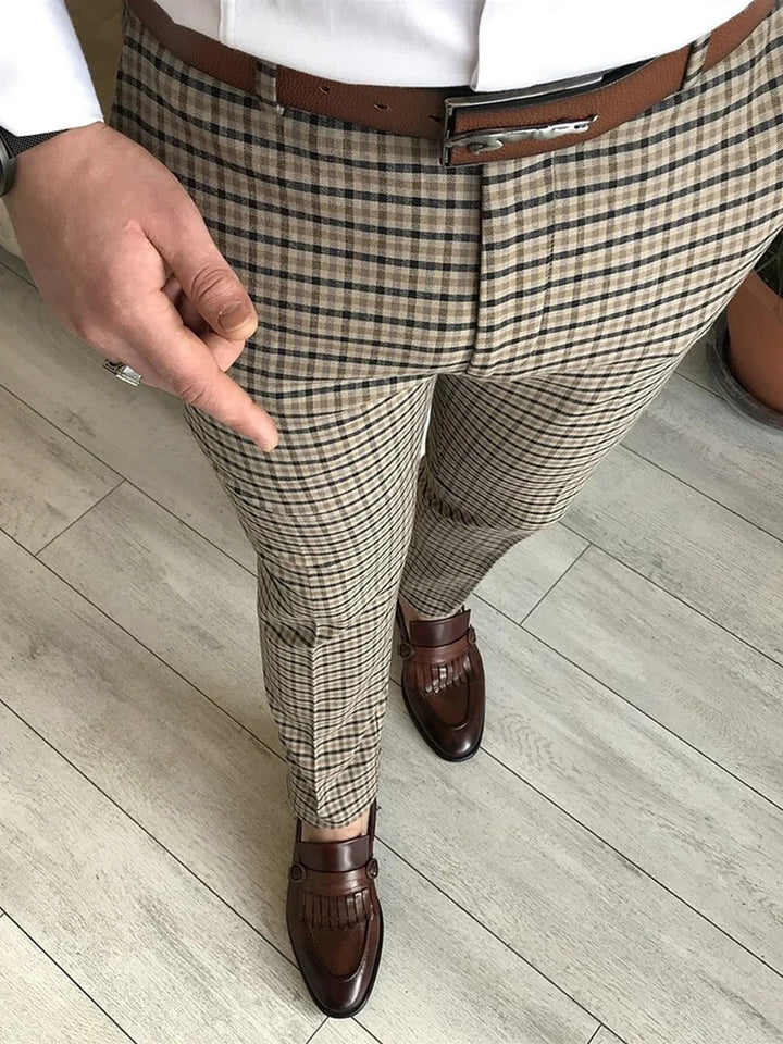 Man wearing beige plaid pants, brown leather belt, and brown tassel loafers on wooden floor
