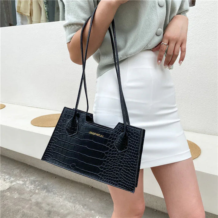 Woman holding black crocodile embossed handbag with long straps, wearing white skirt and light gray top