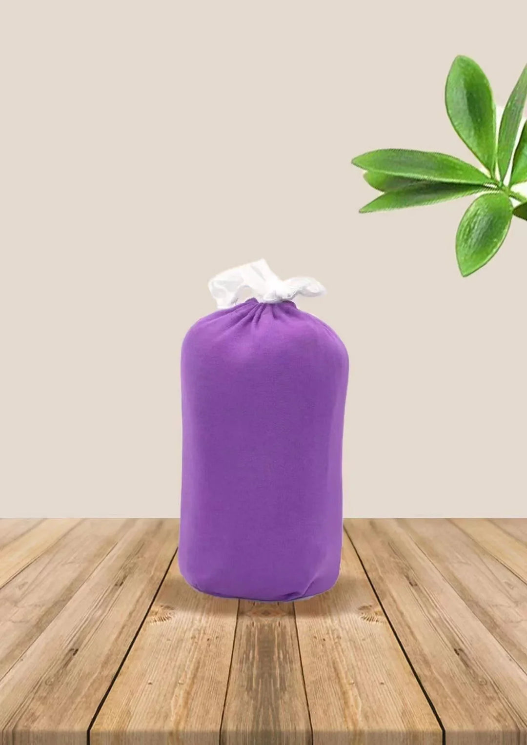 Purple fabric storage bag with white drawstring on wooden table with green leaves in background