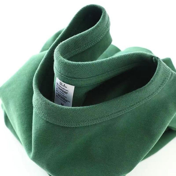 Folded green cotton sweatshirt showing collar and care label on white background