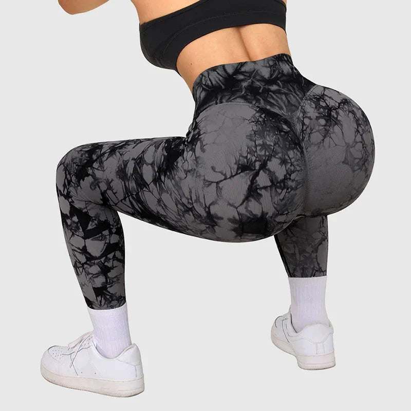 Woman wearing black tie-dye high-waisted leggings and white sneakers in a squatting fitness pose