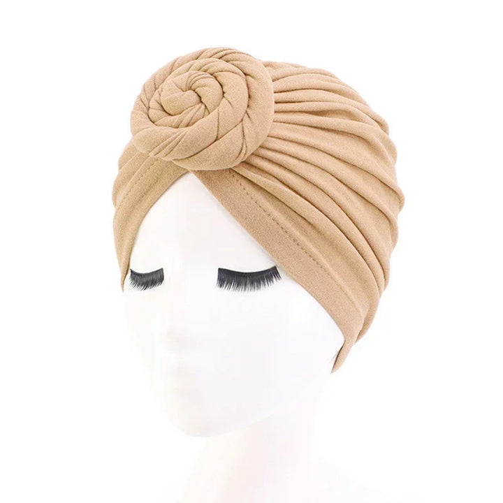 Beige pleated turban headwrap with rose knot detail on white mannequin