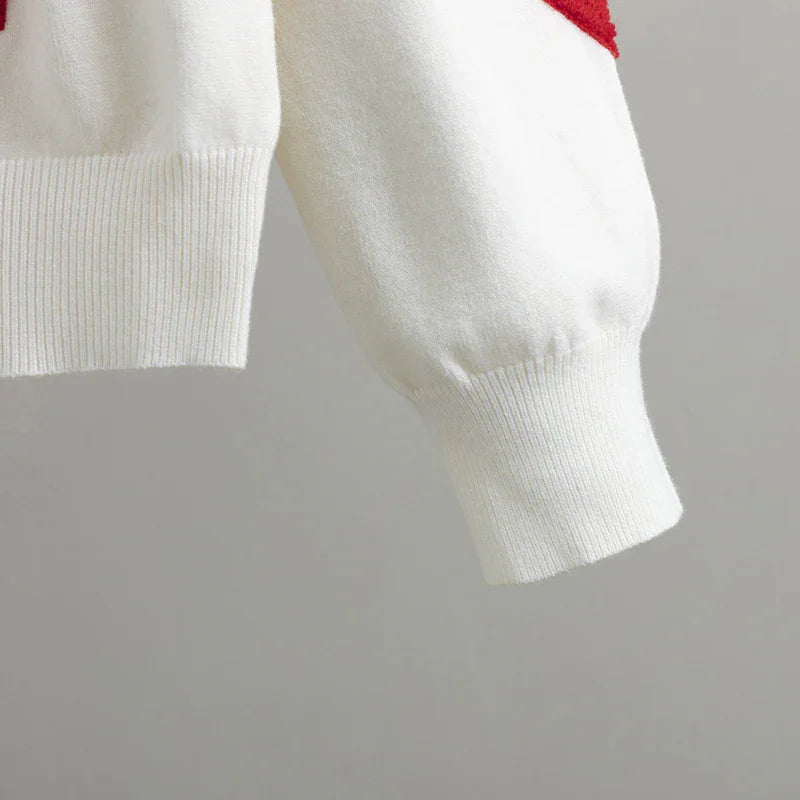 Close-up of white knit sweater sleeve with ribbed cuff and red color detail