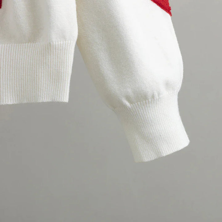 Close-up of white knit sweater sleeve with ribbed cuff and red color detail