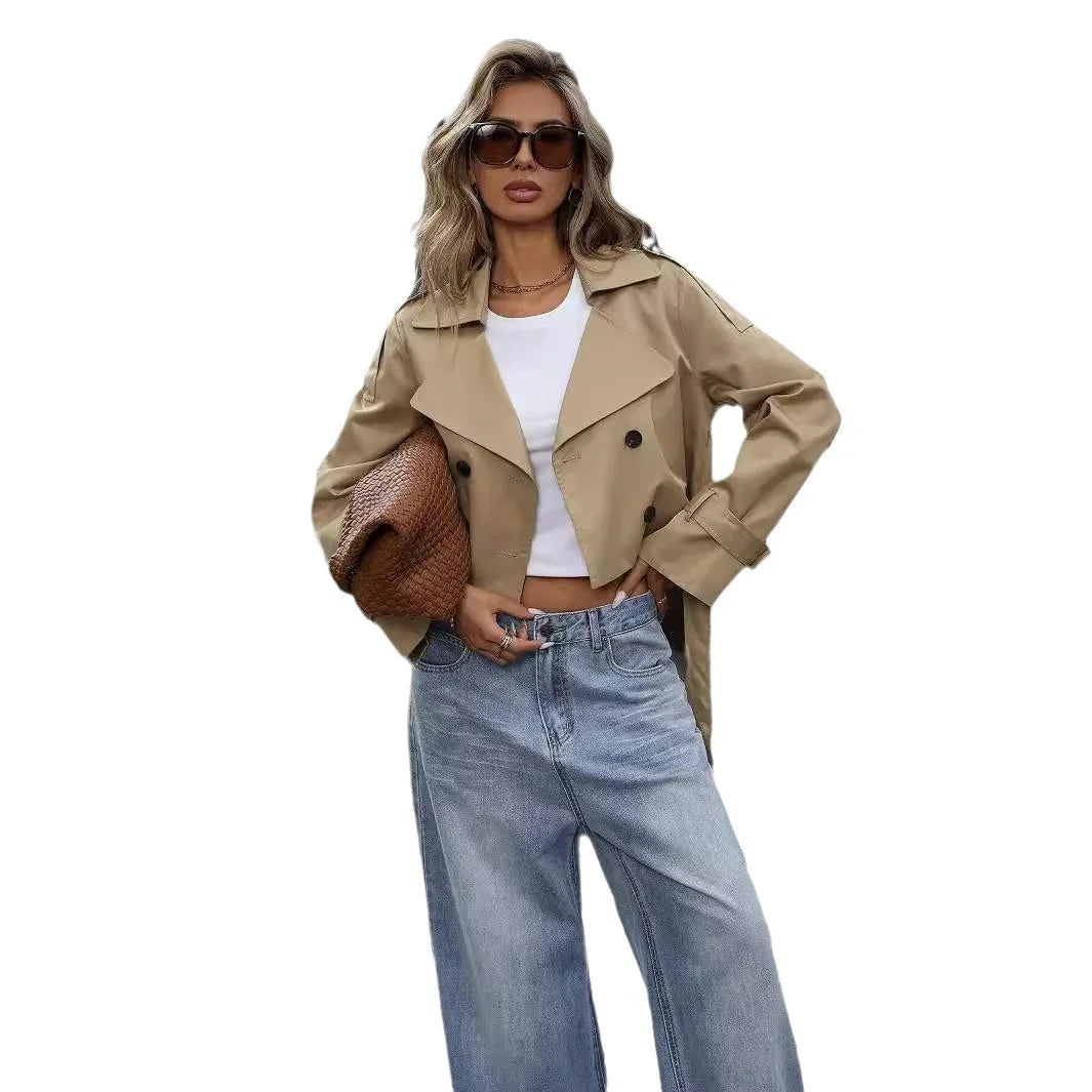 Woman wearing cropped beige trench coat, white tank top, wide-leg jeans, sunglasses, and holding woven clutch