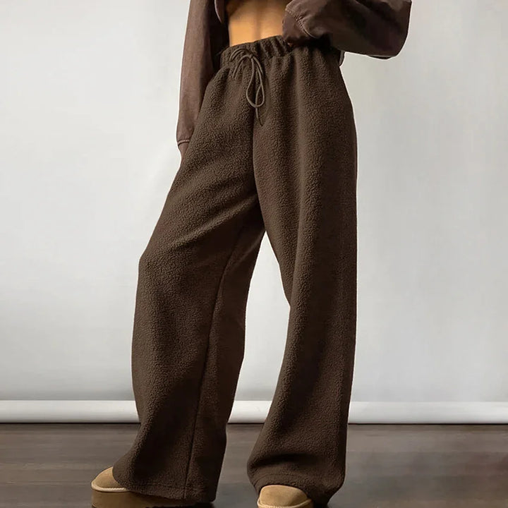 Brown fleece wide-leg lounge pants with drawstring waist, worn with tan shoes on wooden floor