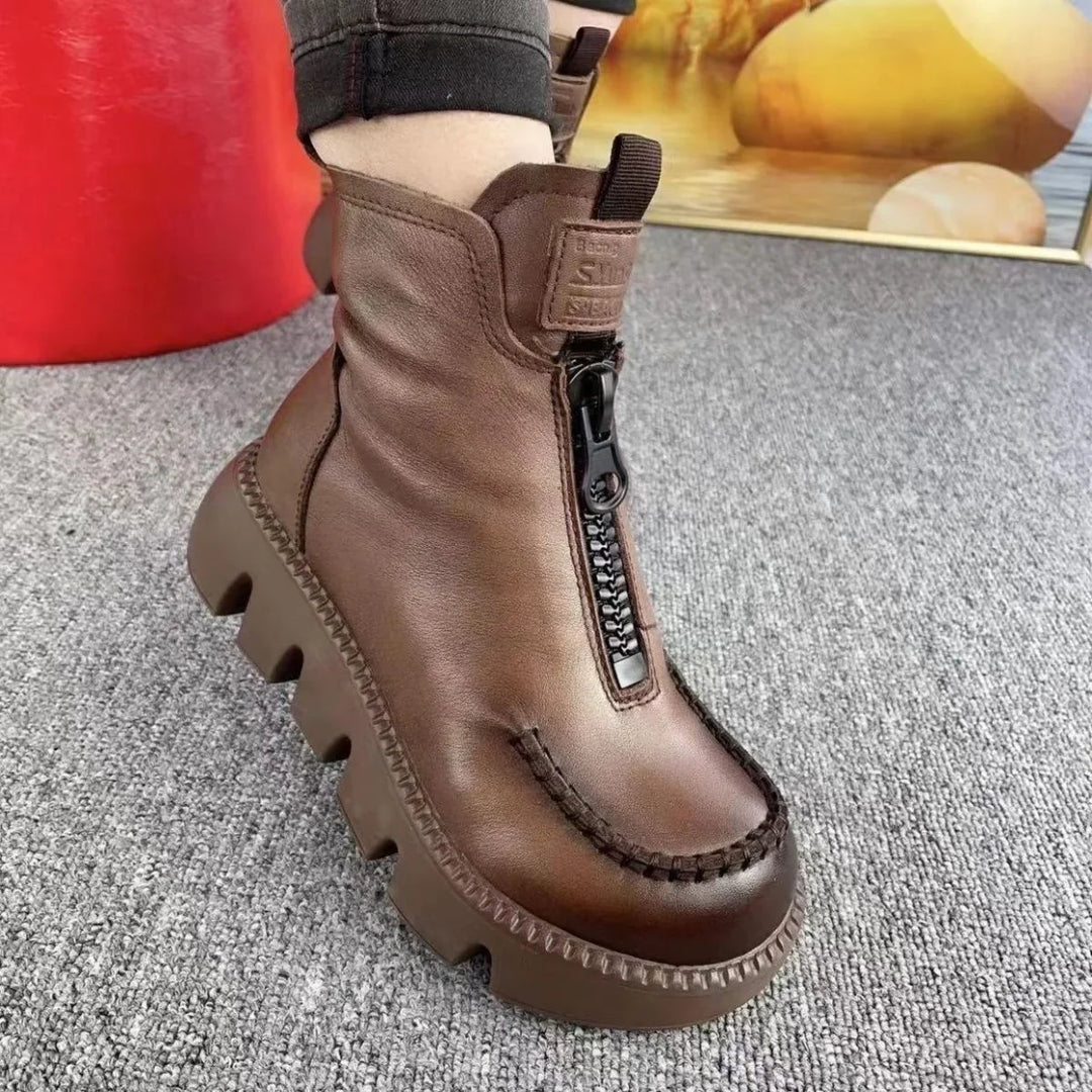 Brown leather platform ankle boot with black front zipper and zigzag sole on grey carpet