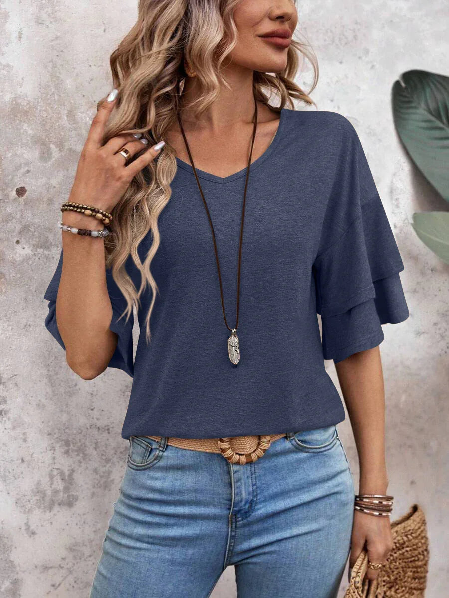 Woman wearing blue tiered ruffle sleeve top with light blue jeans and layered bracelets