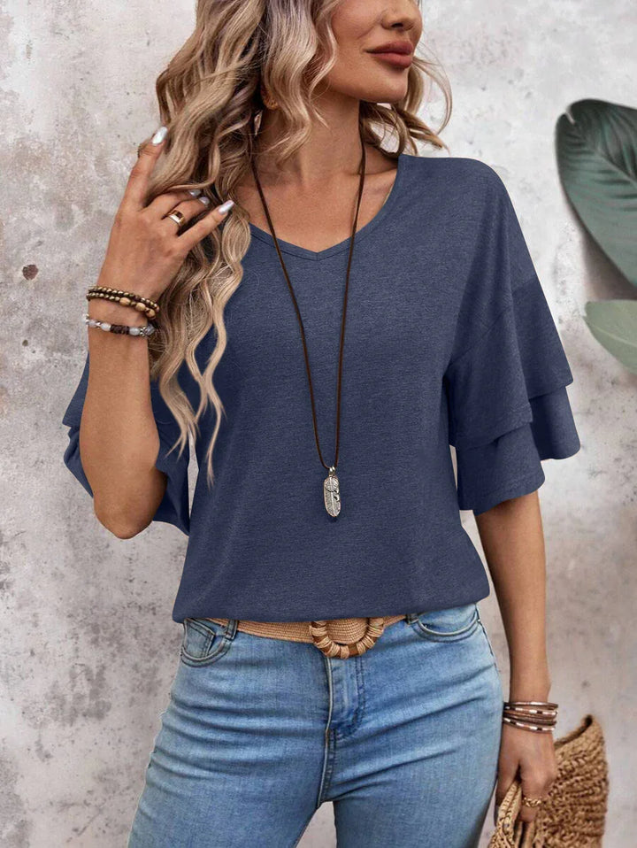 Woman wearing blue tiered ruffle sleeve top with light blue jeans and layered bracelets