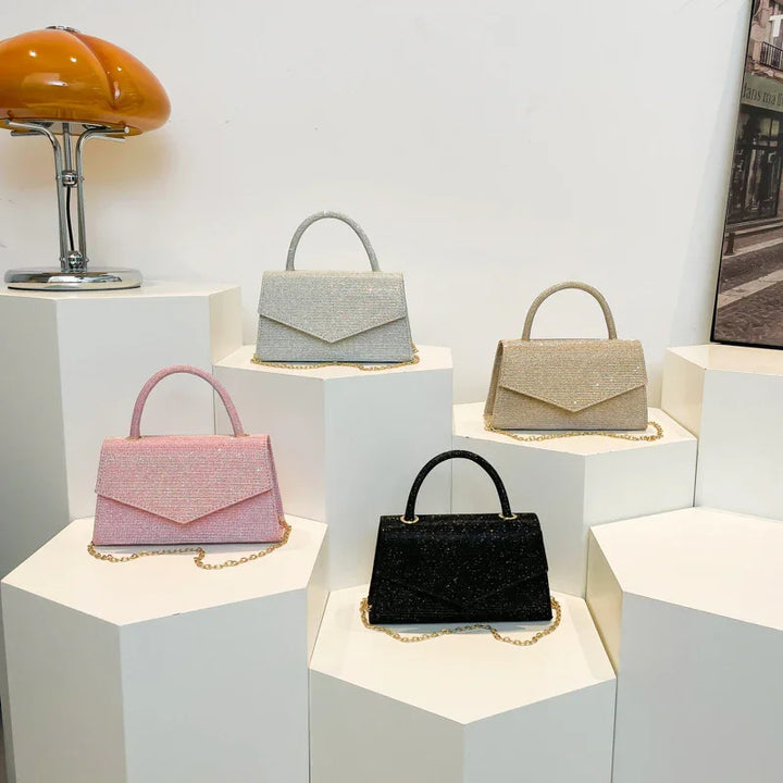 Four elegant textured handbags in pink, white, beige, and black displayed on white geometric pedestals with gold chain straps