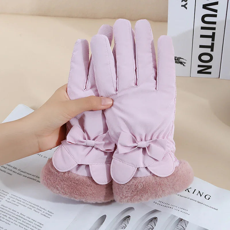 Pair of pink winter gloves with bow detail and faux fur cuffs held in hand on beige background