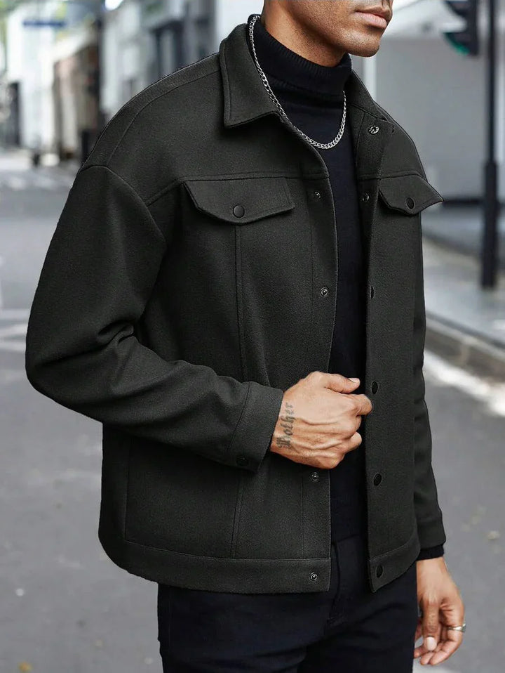 Man wearing black wool jacket with buttoned chest pockets and black turtleneck on city street